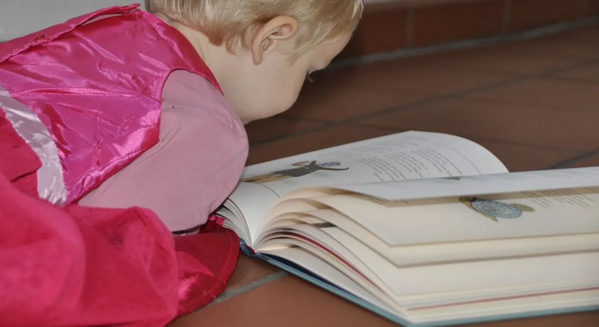 Menina lendo livro no chão. Imagem ilustrativa texto leitura e inteligência.