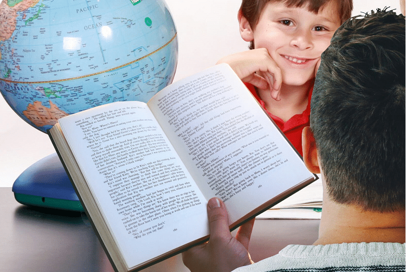 Menino de frente para adulto com livro na mão, com globo terrestre na mesa. Imagem ilustrativa texto biblioterapia.