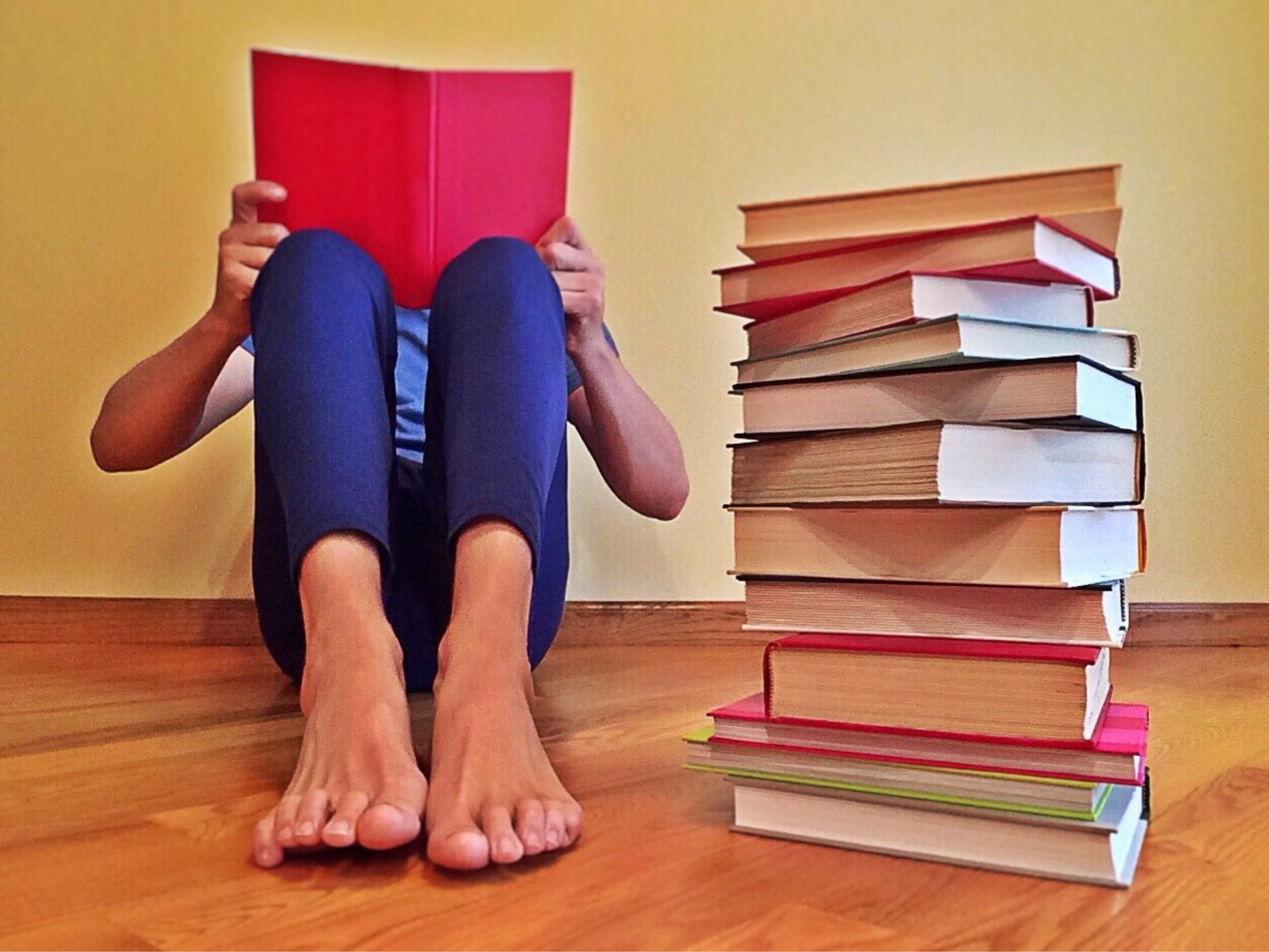 Criança lendo sentada no chão, ao lado de uma pilha de livros. Imagem ilustrativa texto cheiro de livro.