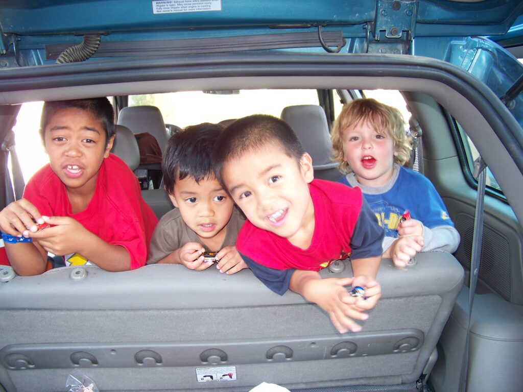 Quatro crianças no banco traseiro de um carro. Imagem ilustrativa texto brincadeiras com as palavras.