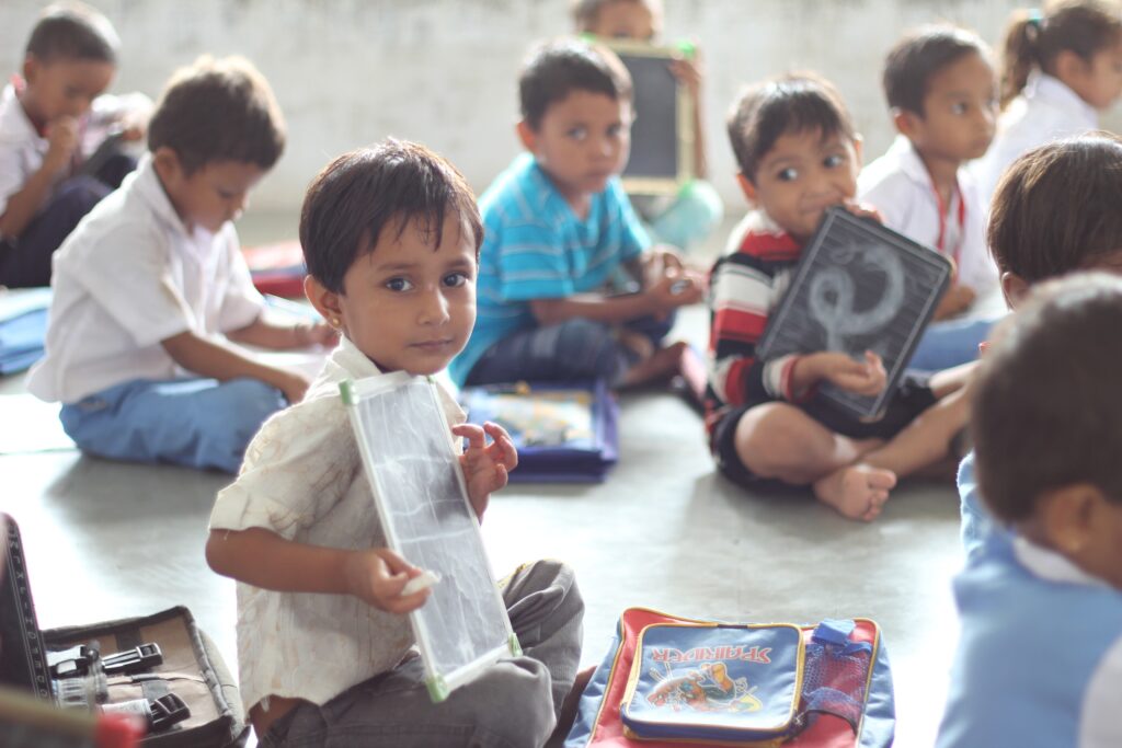 Crianças sentadas no chão, mostrando desenho. Imagem ilustrativa texto educação infantil.
