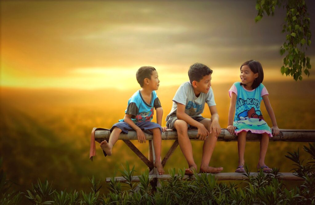 Dois meninos e uma menina sentados do banco, conversando, ao pôr do sol. Imagem ilustrativa texto brincadeiras com as palavras.