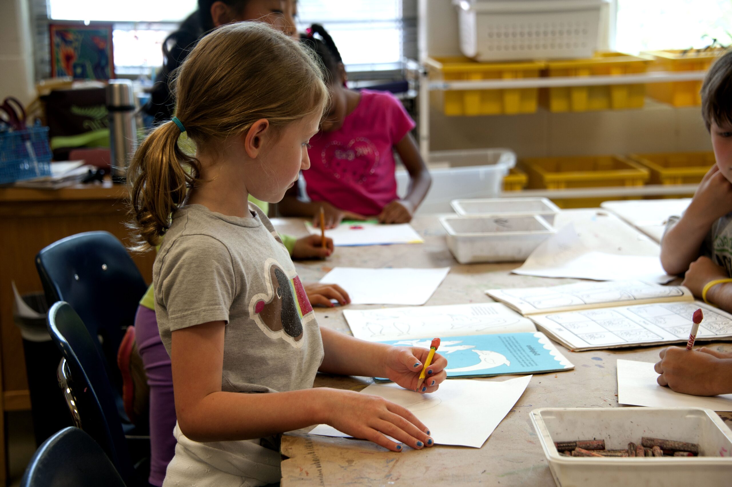 Menina desenhando na escola, com outras crianças. Imagem ilustrativa texto criar histórias em quadrinhos.