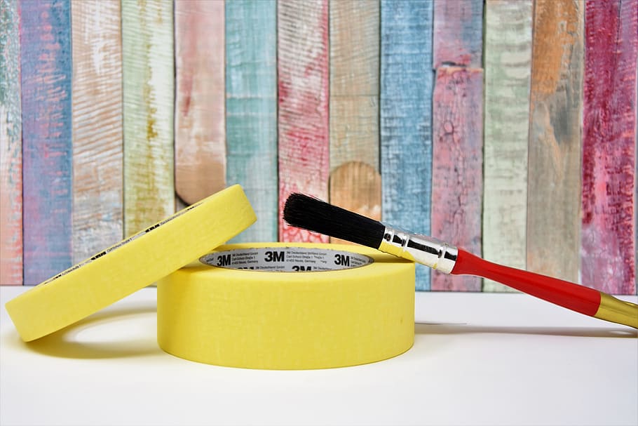 Um rolo de fita crepe sobre o outro, com pincel e fundo colorido de madeira. Imagem ilustrativa texto brincadeiras com fita crepe.