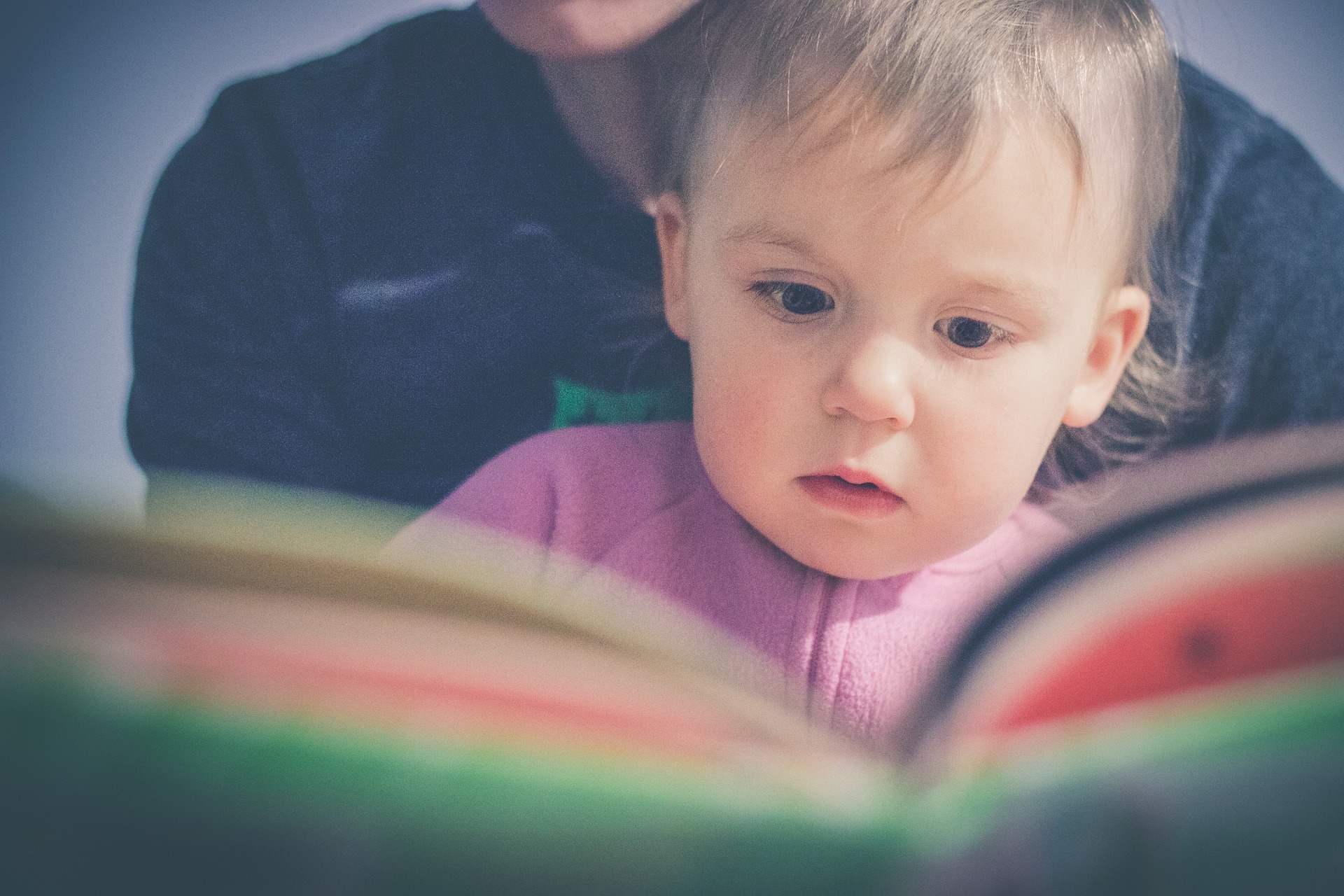Bebê no colo, com livro. Imagem ilustrativa texto livros para cada faixa etária.