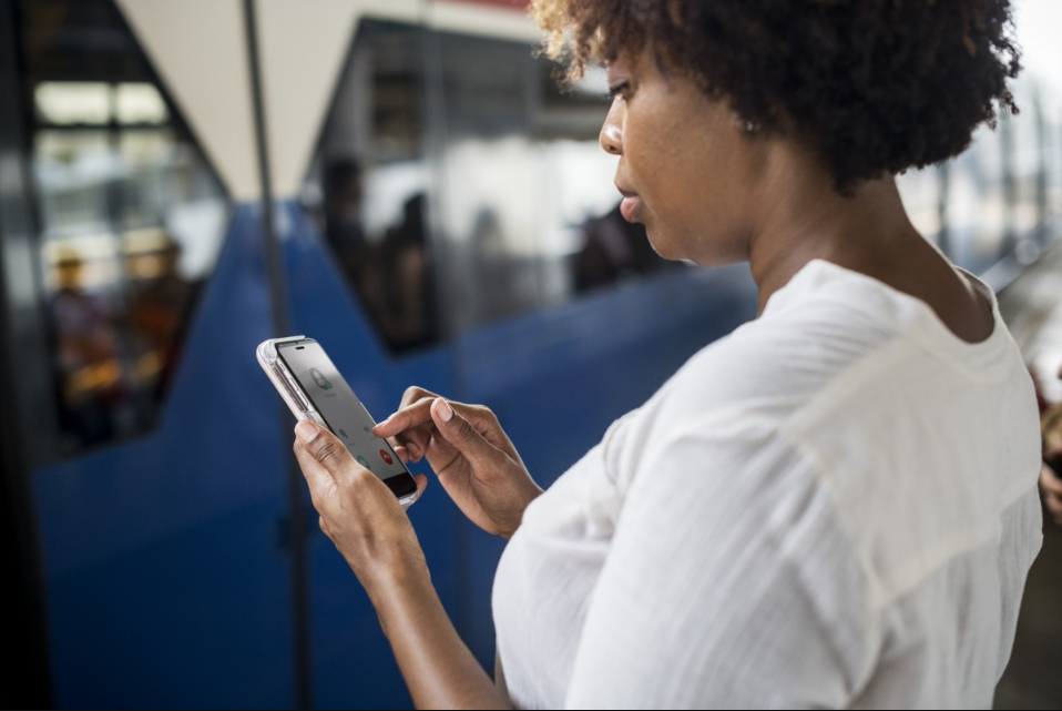 Mulher digitando em celular em estação de metrô. Imagem ilustrativa texto evasão escolar.