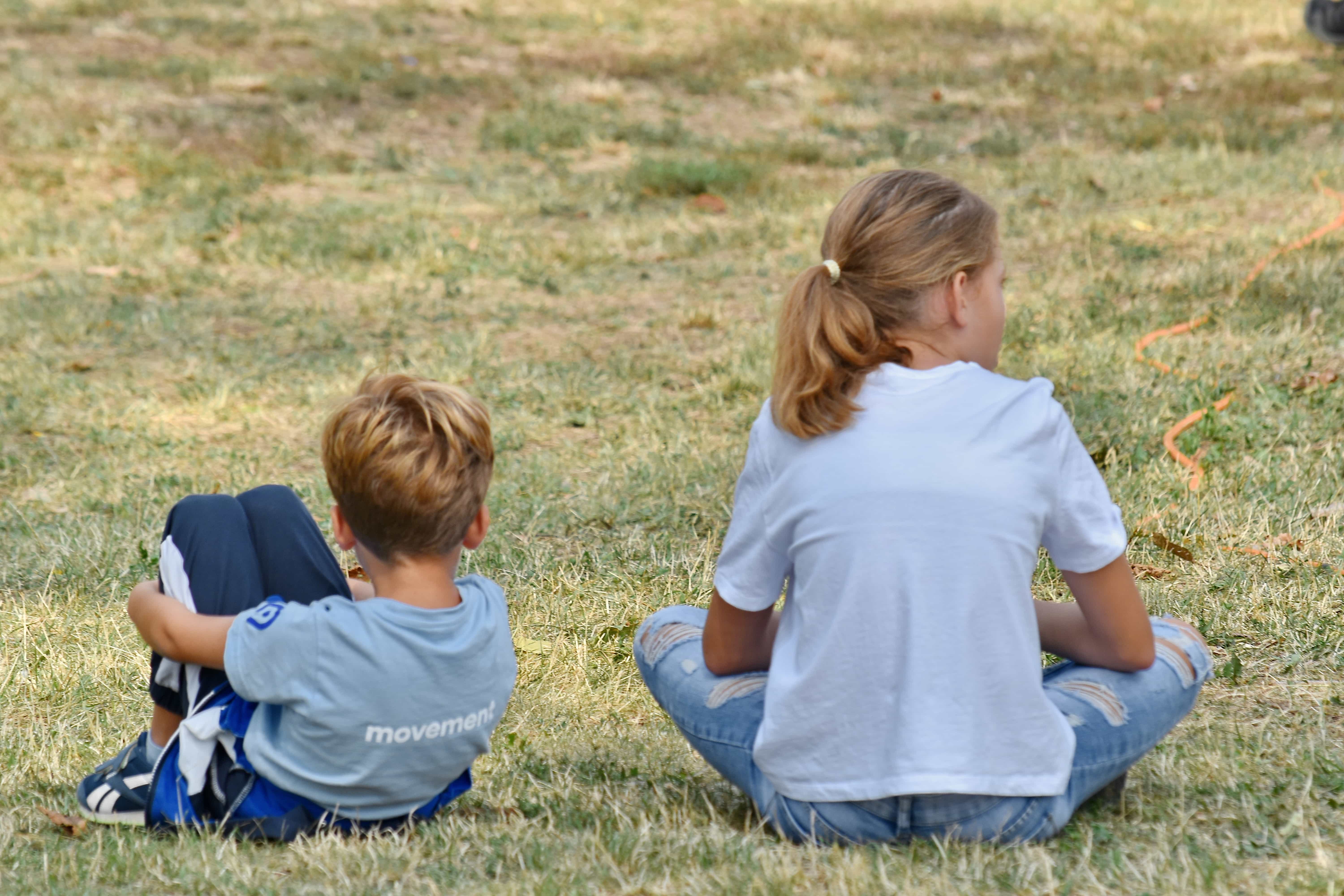 Menino e menina de costas, sentados na grama, olhando para lados opostos. Imagem ilustrativa texto violência não é resposta.