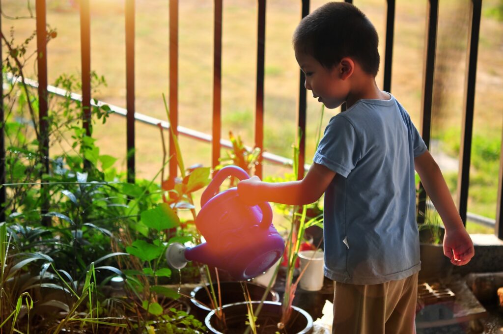 Menino regando plantas. Imagem ilustrativa texto brincar no quintal.