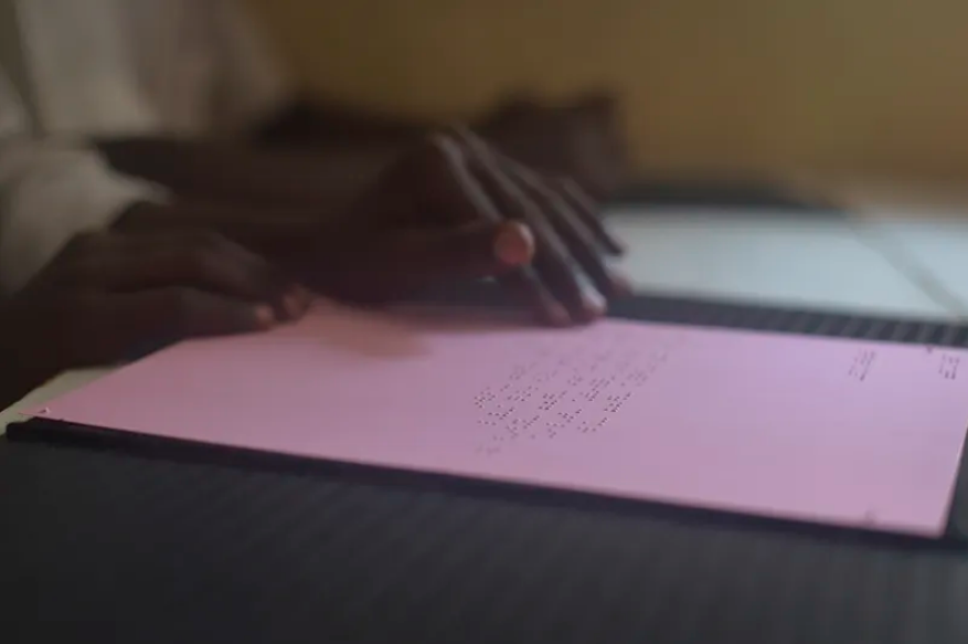Mãos de mulher em papel com escrita em braile. imagem ilustrativa texto acessibilidade linguística.
