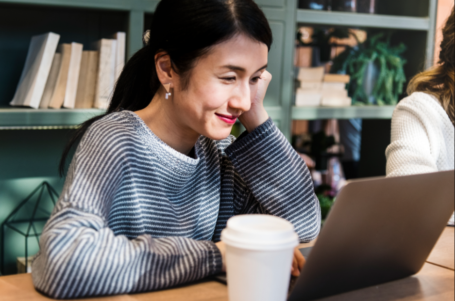 Mulher olhando para o computador, sorrindo. Imagem ilustrativa texto erros de Português.