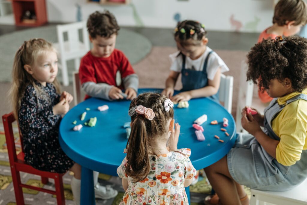 Crianças brincando de massinha na mesa. Imagem ilustrativa texto Reggio Emilia.