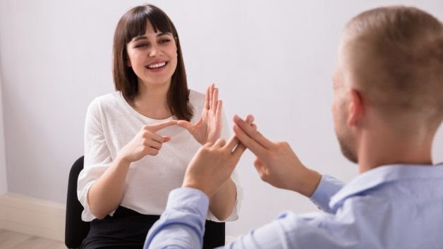 Mulher e homem usando linguagem de sinais (Libras). Imagem ilustrativa texto linguagens do dia a dia.