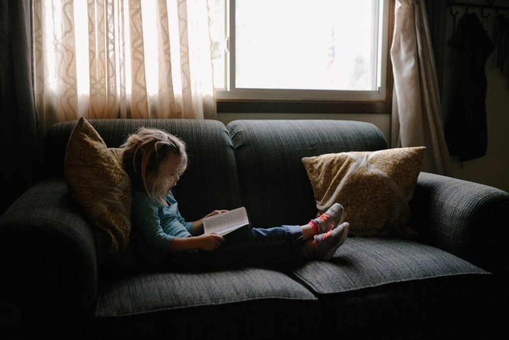 Menina lendo livro no sofá. Imagem ilustrativa texto conhecer autor.