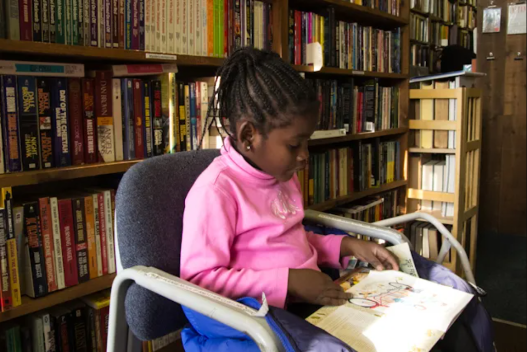 Menina lendo livro na biblioteca. Imagem ilustrativa texto como escolher livros para escola.